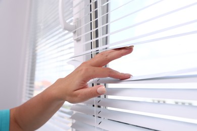 Photo of Woman separating slats of window blinds, closeup