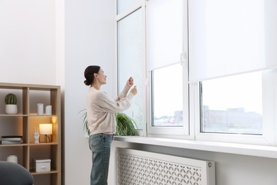 Photo of Woman opening roller blinds on window indoors