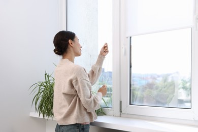 Photo of Woman opening roller blinds on window indoors