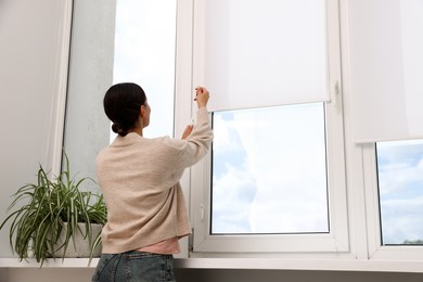 Photo of Woman opening roller blinds on window indoors