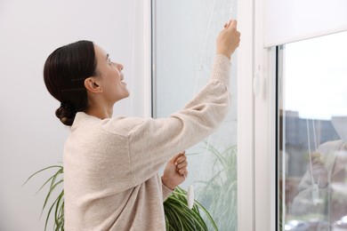 Photo of Woman opening roller blinds on window indoors