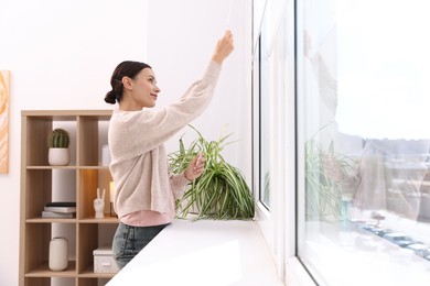 Photo of Woman opening roller blinds on window indoors