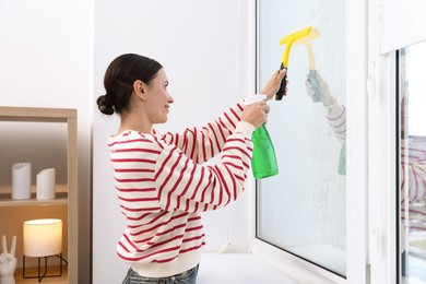 Photo of Woman cleaning window with squeegee and detergent indoors