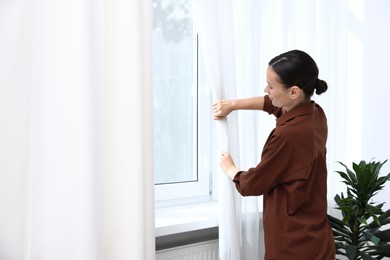 Photo of Woman opening curtains and looking out of window indoors