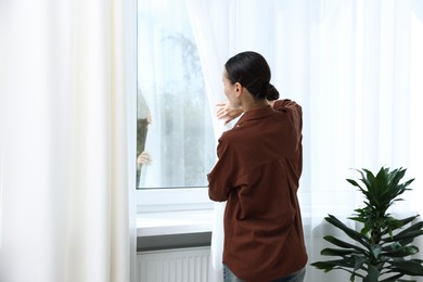 Photo of Woman opening curtains and looking out of window indoors