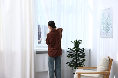 Photo of Woman opening curtains and looking out of window indoors