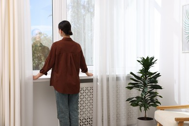 Photo of Woman looking out of window indoors, back view
