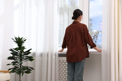 Photo of Woman looking out of window indoors, back view