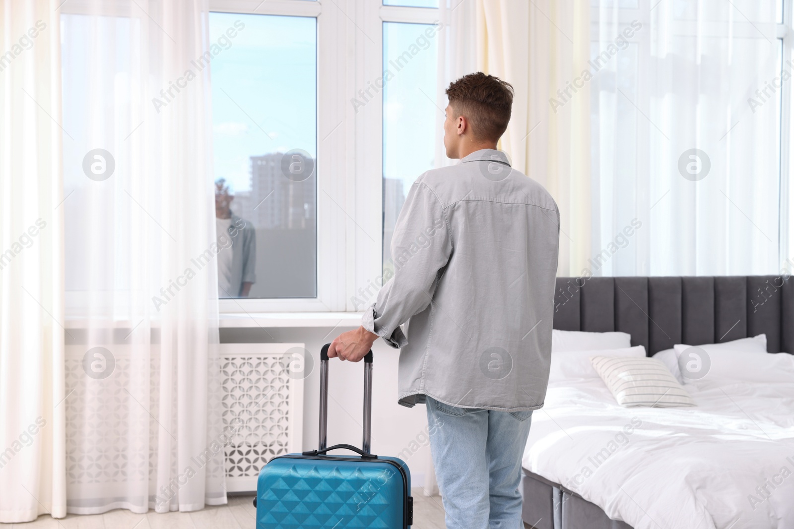 Photo of Man with suitcase looking out window indoors, back view