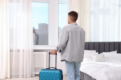 Photo of Man with suitcase looking out window indoors, back view