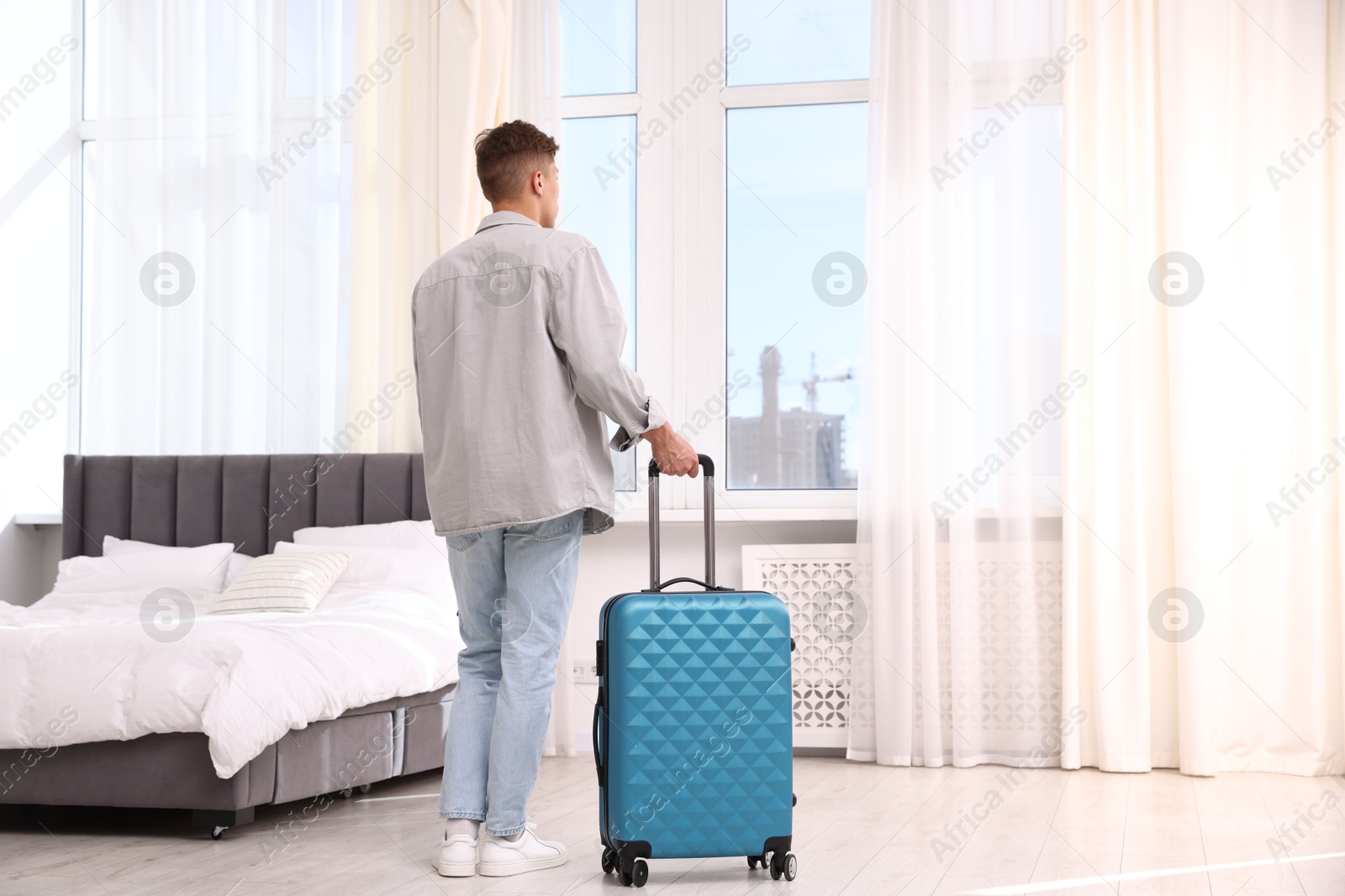 Photo of Man with suitcase looking out window indoors, back view