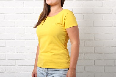 Photo of Young woman wearing stylish yellow t-shirt near white brick wall, closeup. Mockup for design