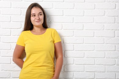 Photo of Young woman wearing stylish yellow t-shirt near white brick wall. Mockup for design