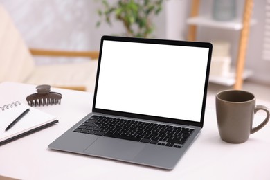 Photo of Modern laptop with blank screen, cup of coffee and notebook on white table indoors. Mockup for design