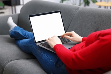 Photo of Woman working with laptop on sofa indoors, closeup. Mockup for design