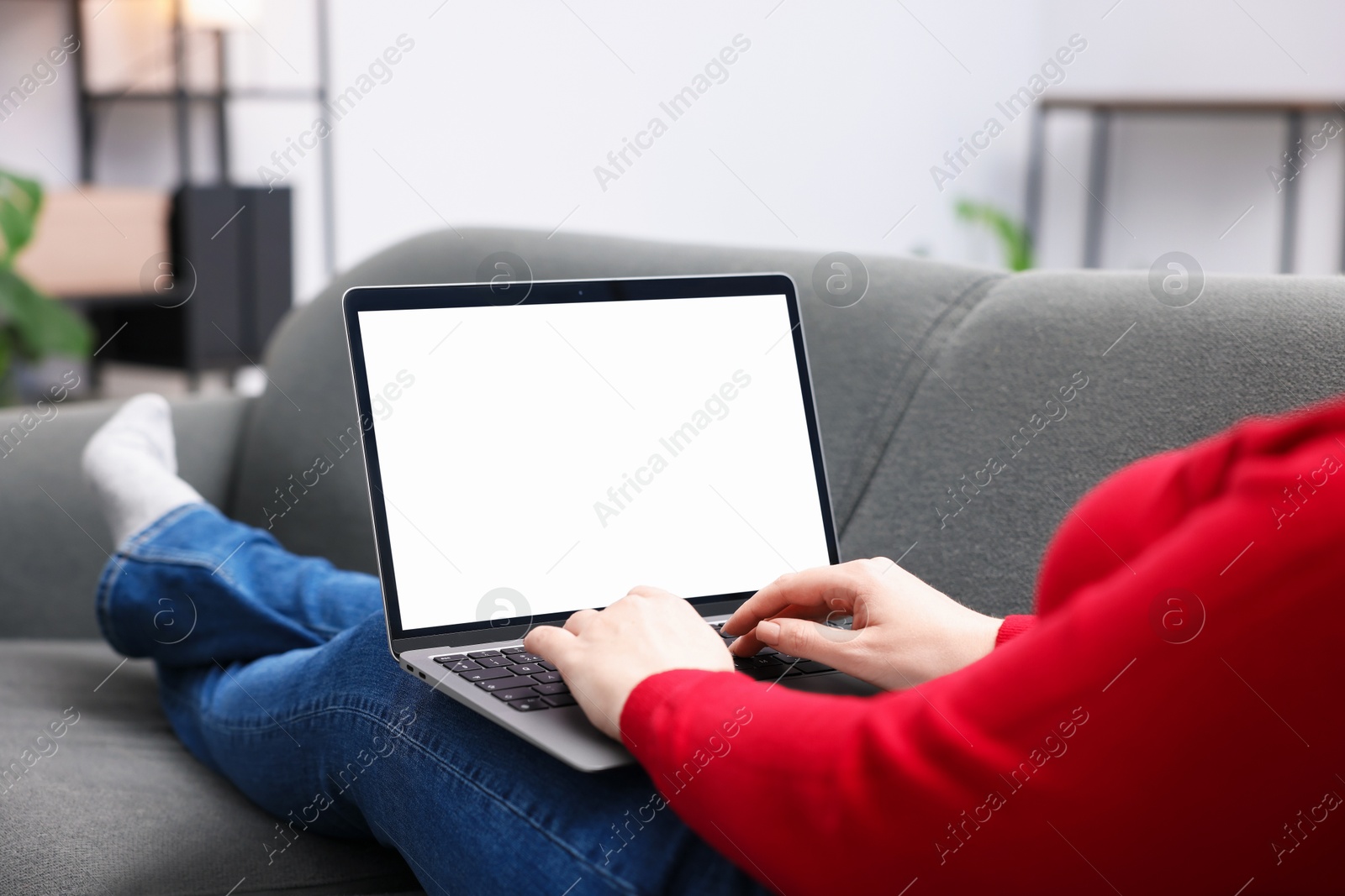 Photo of Woman working with laptop on sofa indoors, closeup. Mockup for design