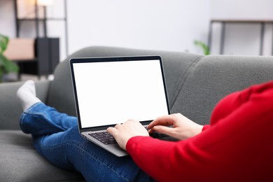 Photo of Woman working with laptop on sofa indoors, closeup. Mockup for design