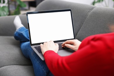 Photo of Woman working with laptop on sofa indoors, closeup. Mockup for design