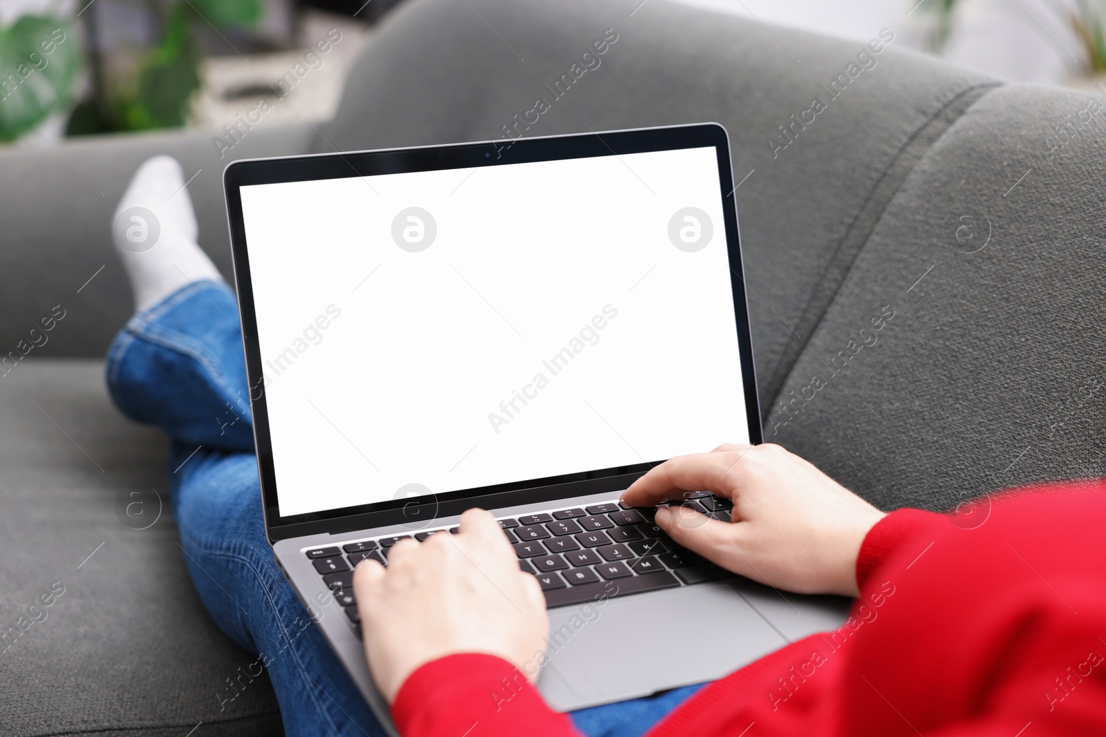 Photo of Woman working with laptop on sofa indoors, closeup. Mockup for design