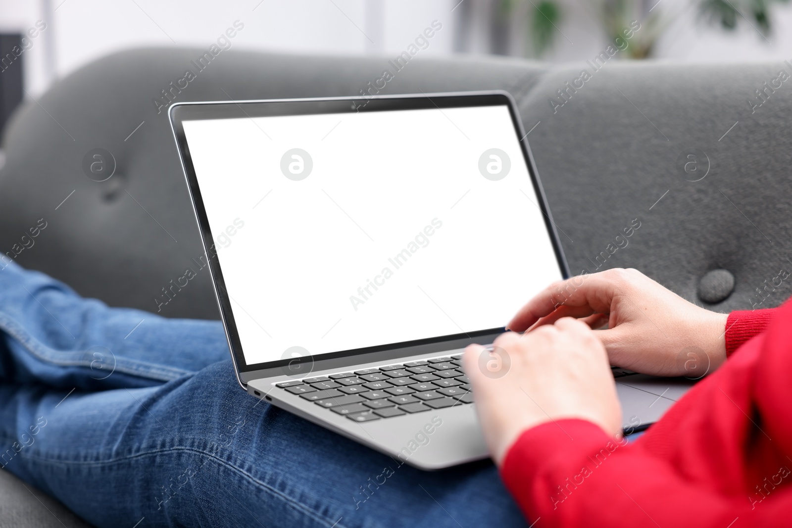 Photo of Woman working with laptop on sofa indoors, closeup. Mockup for design