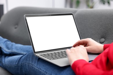 Photo of Woman working with laptop on sofa indoors, closeup. Mockup for design
