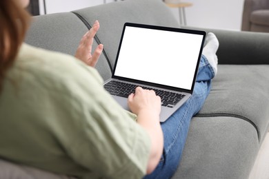 Photo of Woman working with laptop on sofa indoors, closeup. Mockup for design
