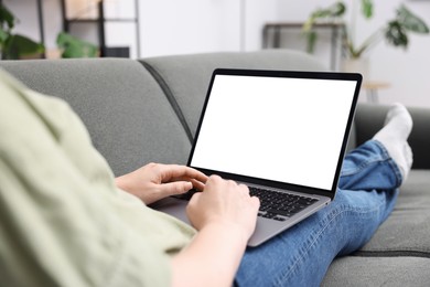 Photo of Woman working with laptop on sofa indoors, closeup. Mockup for design