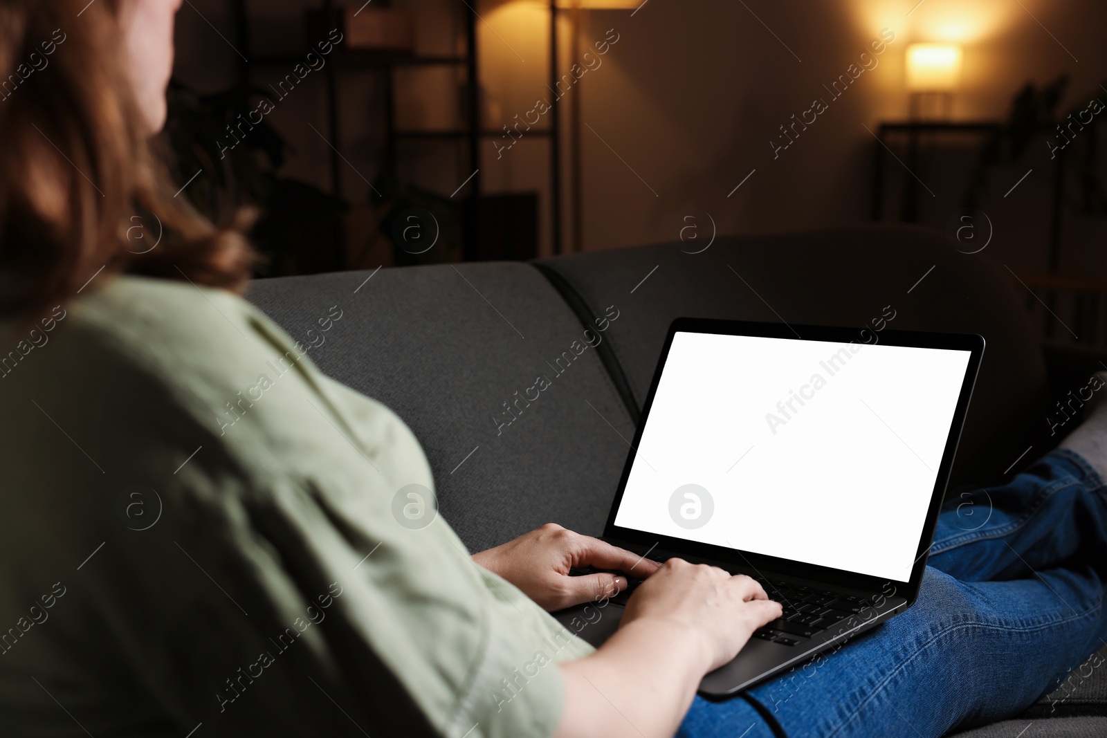Photo of Woman working with laptop on sofa indoors, closeup. Mockup for design
