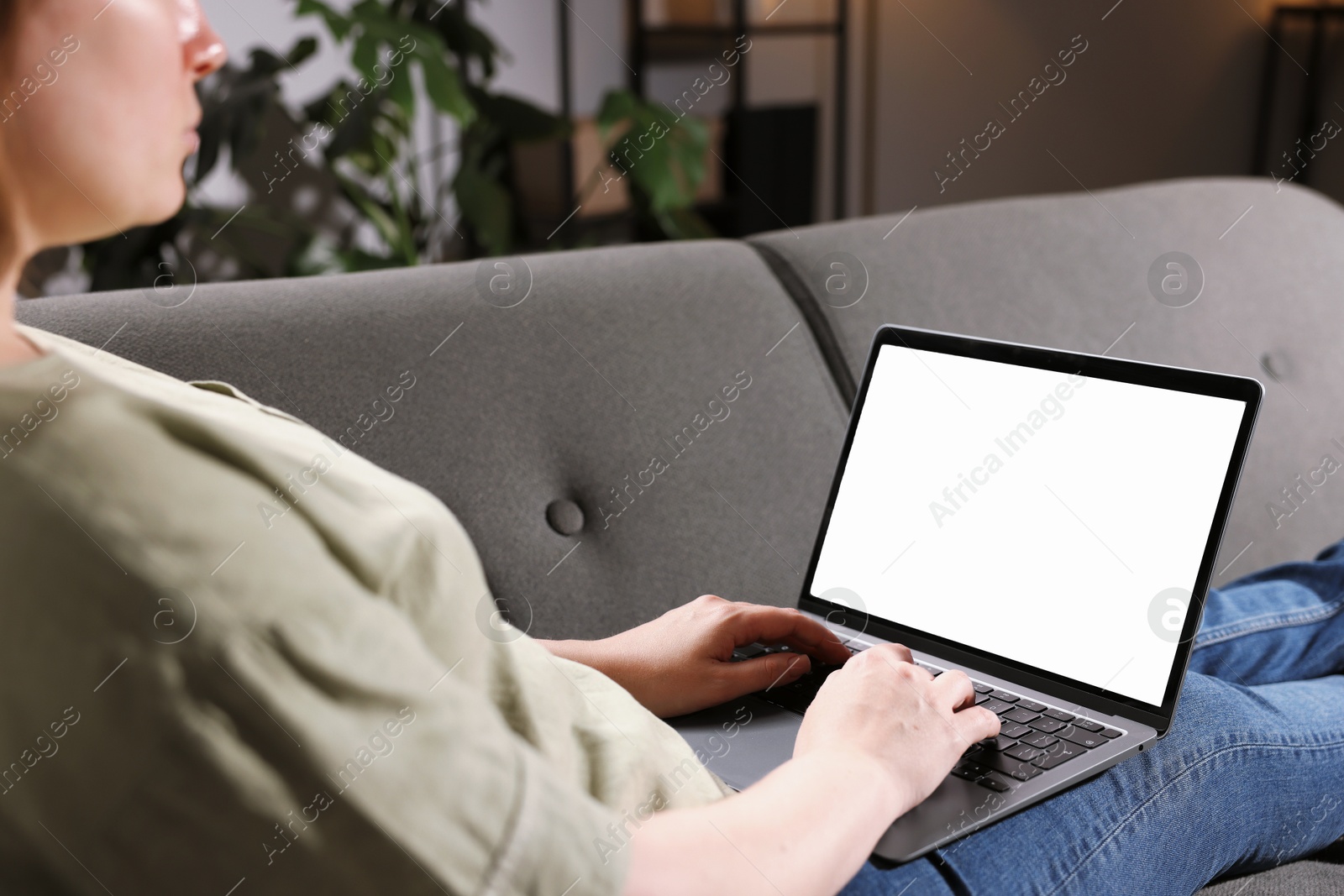 Photo of Woman working with laptop on sofa indoors, closeup. Mockup for design