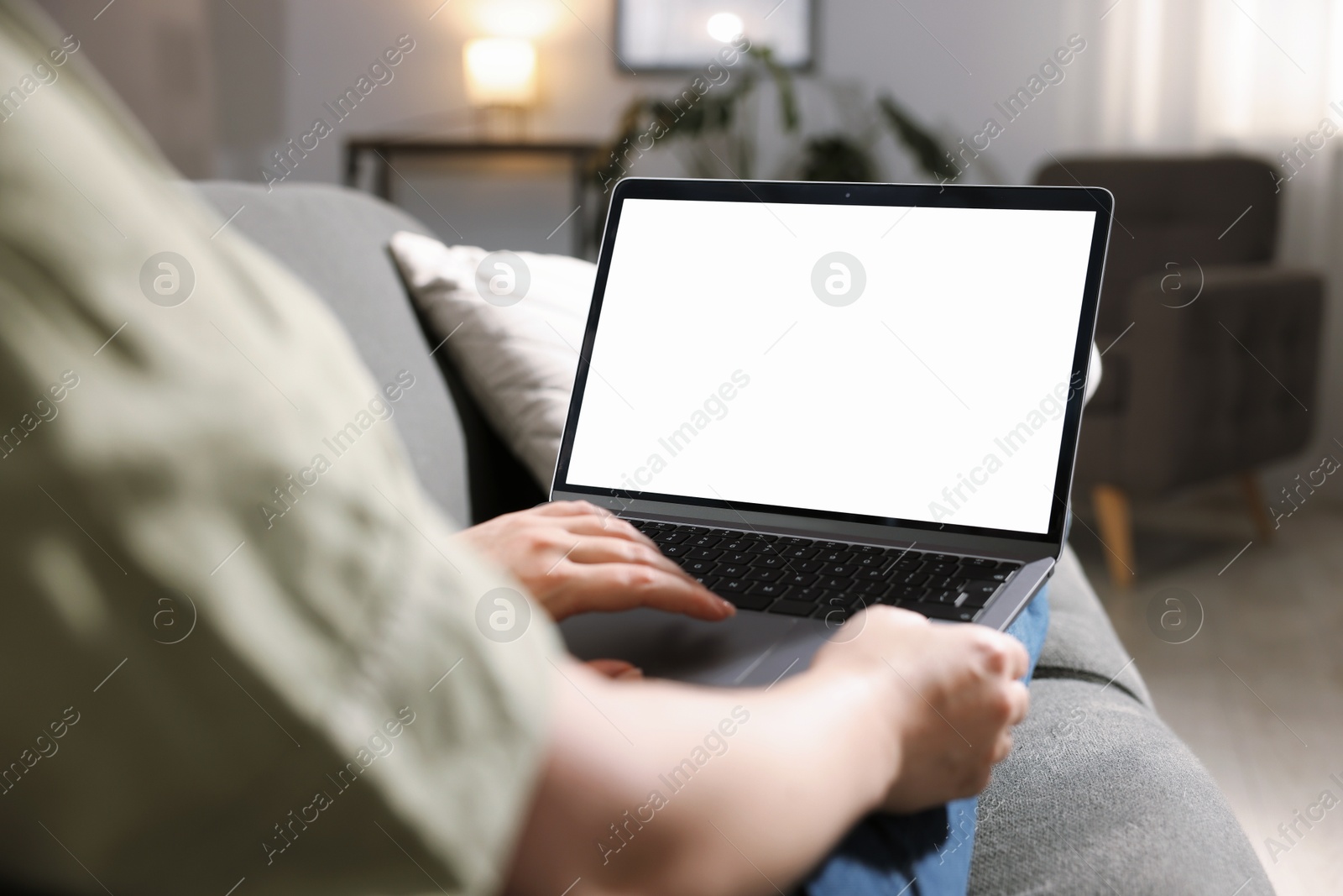Photo of Woman working with laptop on sofa indoors, closeup. Mockup for design
