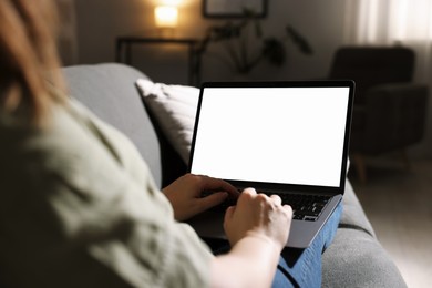 Photo of Woman working with laptop on sofa indoors, closeup. Mockup for design