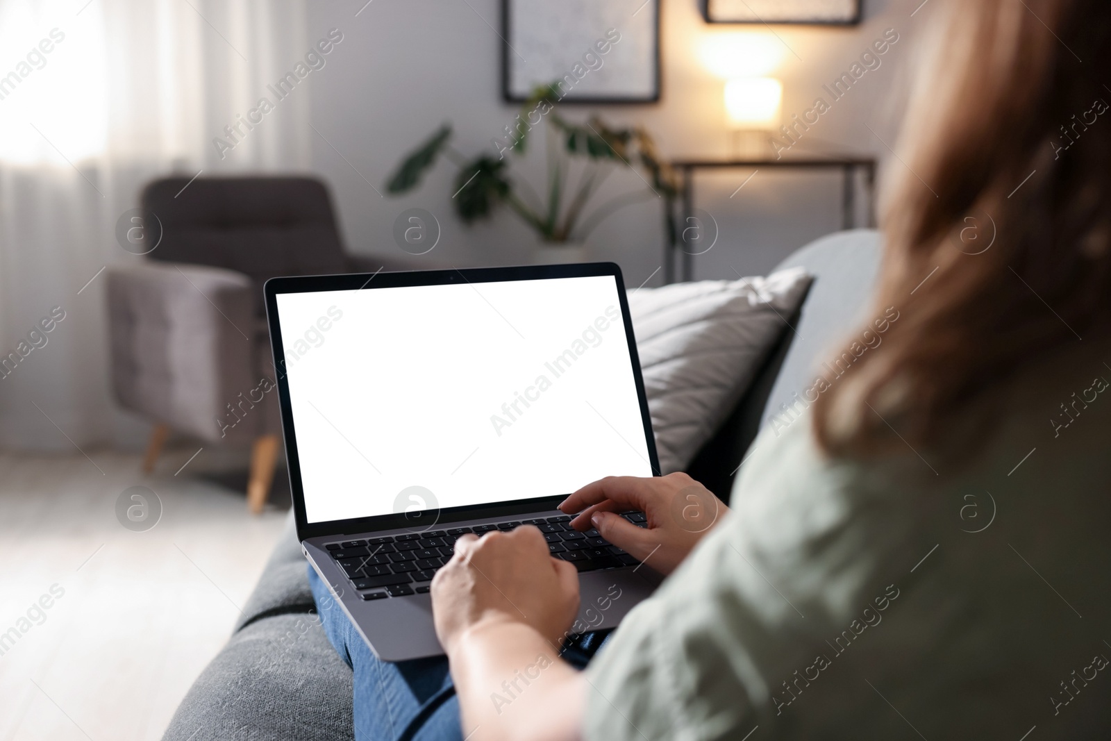 Photo of Woman working with laptop on sofa indoors, closeup. Mockup for design
