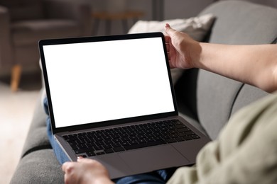 Photo of Woman working with laptop on sofa indoors, closeup. Mockup for design