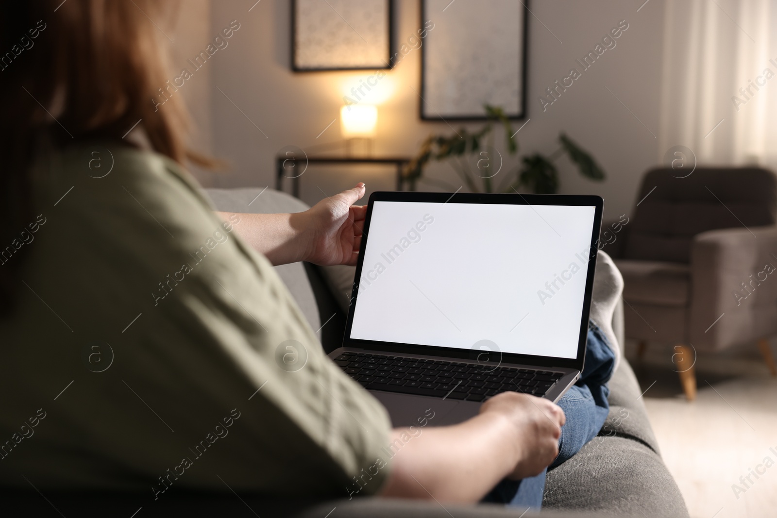Photo of Woman working with laptop on sofa indoors, closeup. Mockup for design
