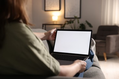 Photo of Woman working with laptop on sofa indoors, closeup. Mockup for design