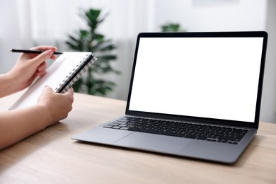 Photo of Woman working with laptop at wooden table indoors, closeup. Mockup for design