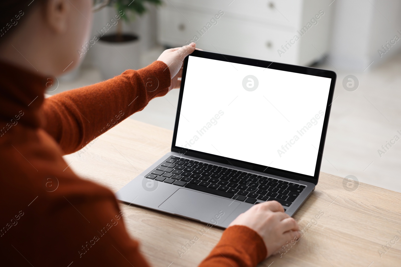 Photo of Woman working with laptop at wooden table indoors, closeup. Mockup for design