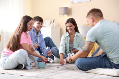 Photo of Group of friends playing cards on floor indoors