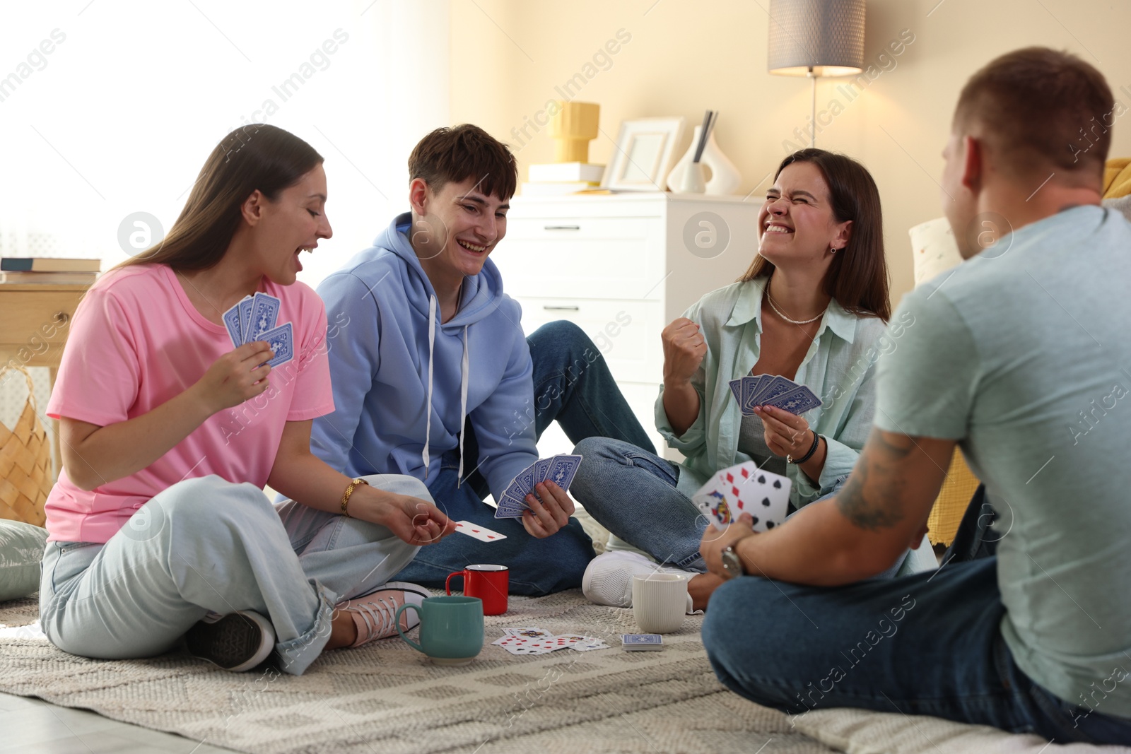 Photo of Group of friends playing cards on floor indoors