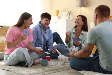 Photo of Group of friends playing cards on floor indoors