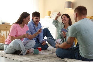 Photo of Group of friends playing cards on floor indoors