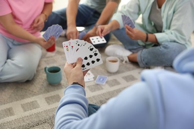 Photo of Group of friends playing cards on floor indoors, closeup