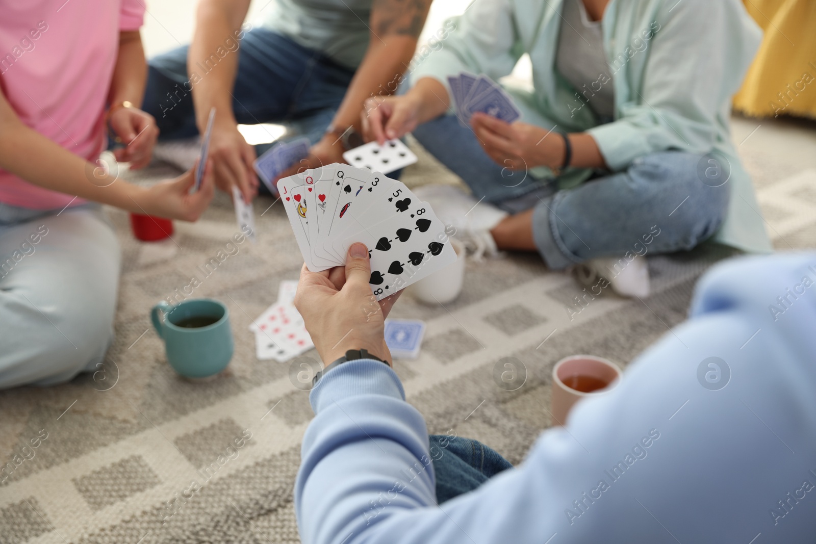 Photo of Group of friends playing cards on floor indoors, closeup