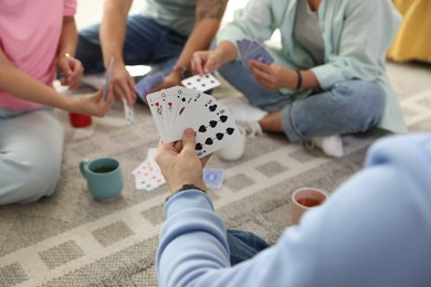 Photo of Group of friends playing cards on floor indoors, closeup