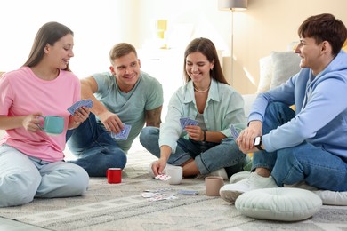 Photo of Group of friends playing cards on floor indoors