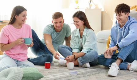 Photo of Group of friends playing cards on floor indoors