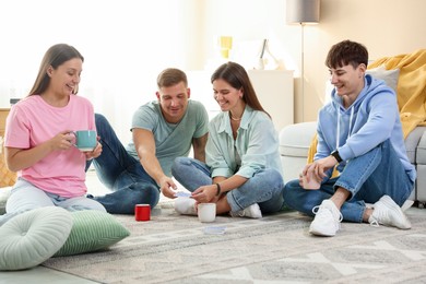 Photo of Group of friends playing cards on floor indoors