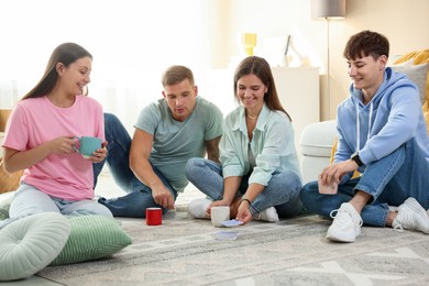 Photo of Group of friends playing cards on floor indoors