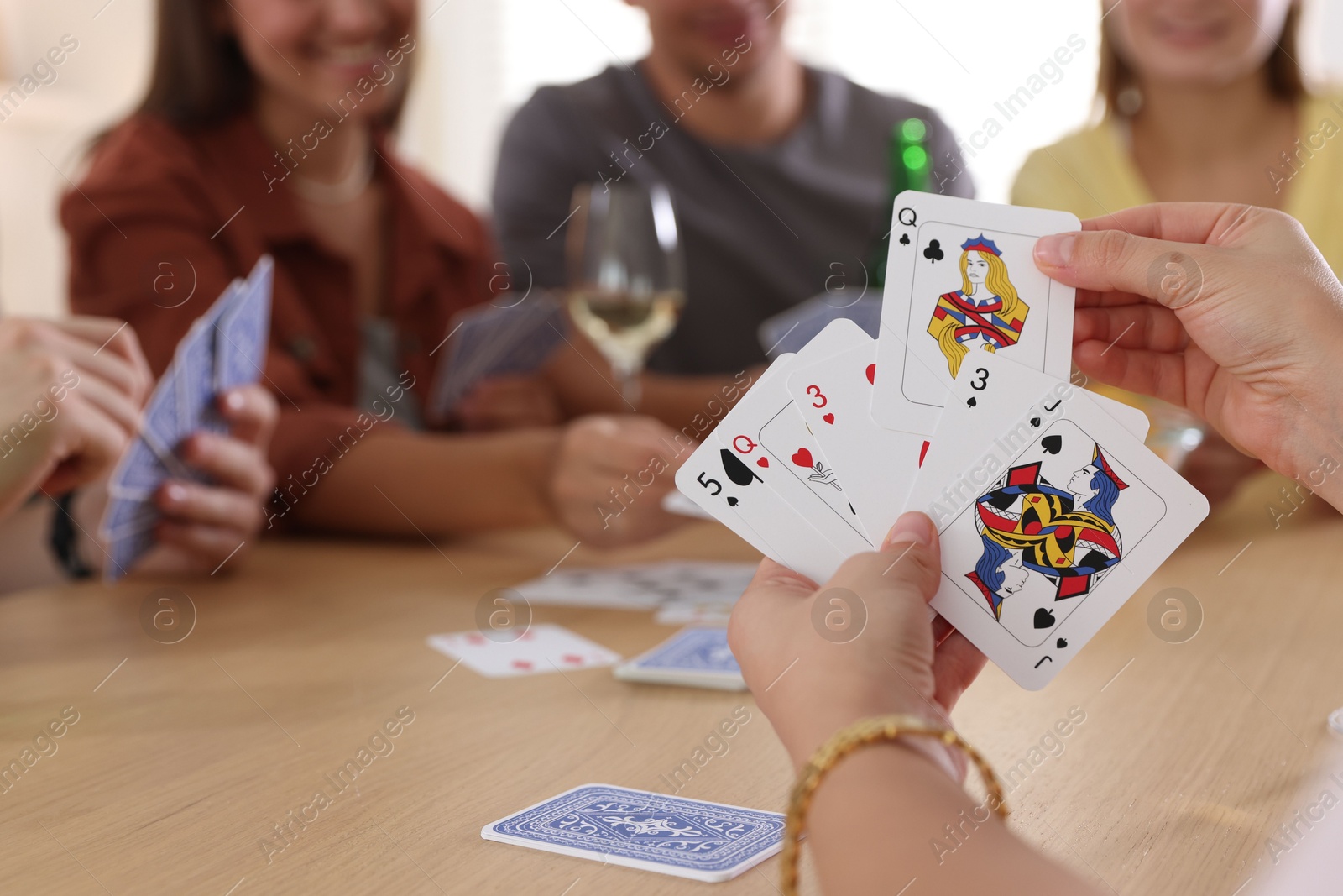 Photo of Group of friends playing cards at wooden table indoors, selective focus