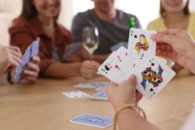 Photo of Group of friends playing cards at wooden table indoors, selective focus